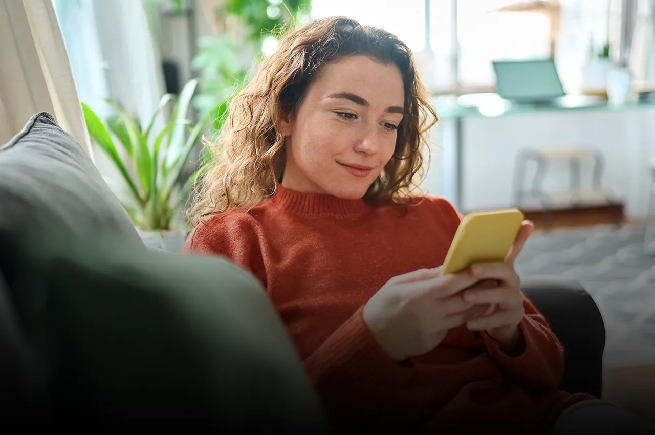 Frau zuhause mit Handy in der Hand